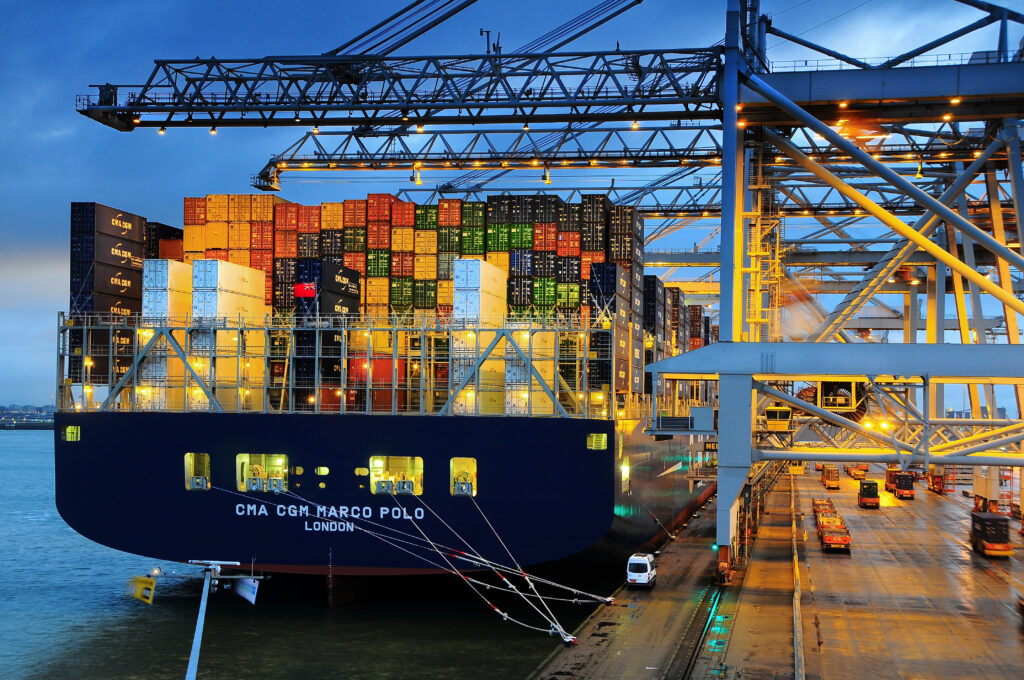 Schip in de containerterminal waar containers op en af het schip geladen worden door de kranen in de avond.